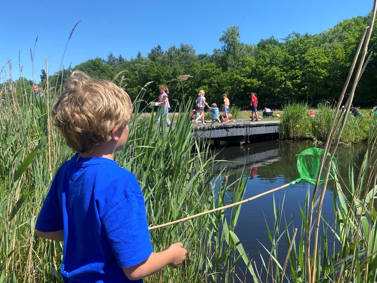 Jongen met schepnet bij het water, kinderen op een vlonder op de achtergrond