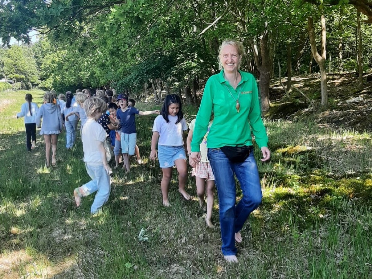 Renske wandelt lachend met een groep kinderen door het groen